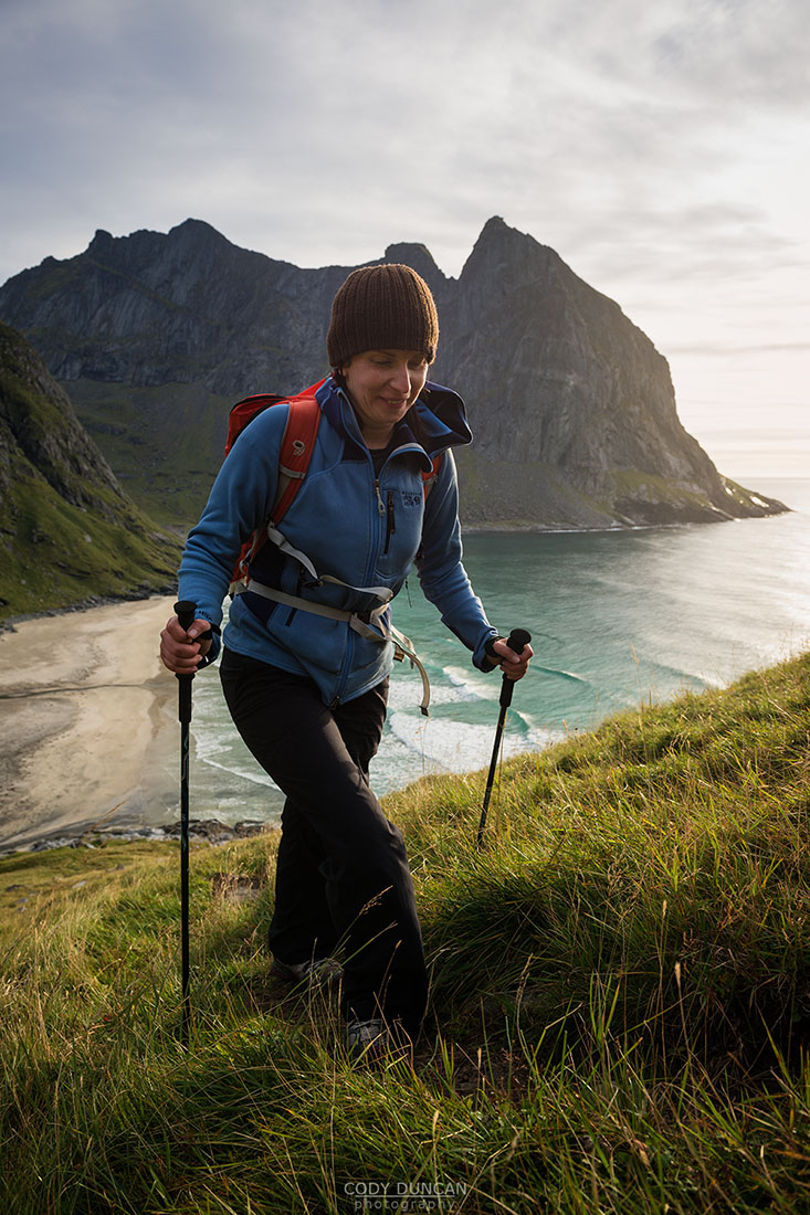 Female hiker hiking up trail with Kvalvika beach in background, Moskenesoy, Lofoten Islands, Norway